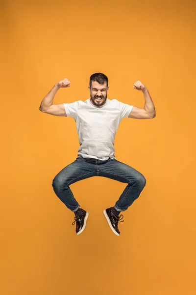 Свобода передвижения. Красивый молодой человек прыгает на оранжевом фоне — стоковое фото