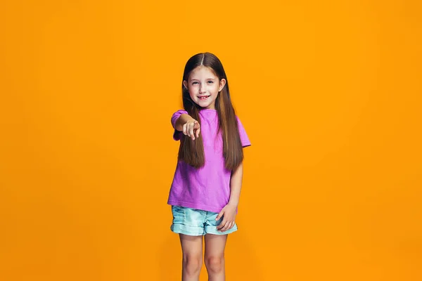 La chica adolescente feliz que apunta a usted, media longitud primer plano retrato sobre fondo naranja . — Foto de Stock