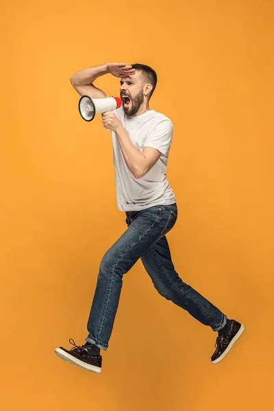 Jumping fan on orange background. The young man as soccer football fan with megaphone — Stock Photo, Image