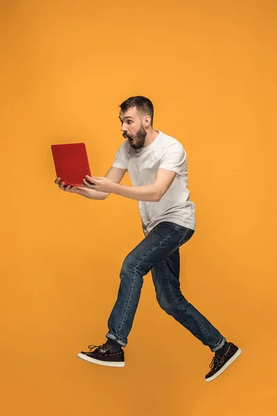 Образ молодого чоловіка над помаранчевим тлом за допомогою ноутбука під час стрибків . — стокове фото