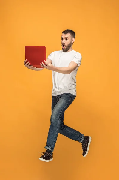Immagine di giovane uomo su sfondo arancione utilizzando computer portatile durante il salto . — Foto Stock