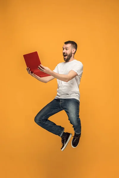 점프 하는 동안 랩톱 컴퓨터를 사용 하는 주황색 배경 위에 젊은 남자의 이미지. — 스톡 사진