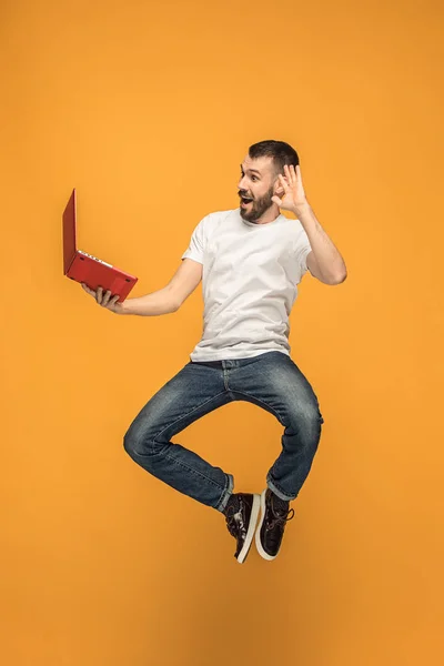 Afbeelding van de jonge man over oranje achtergrond met behulp van laptopcomputer tijdens het springen. — Stockfoto