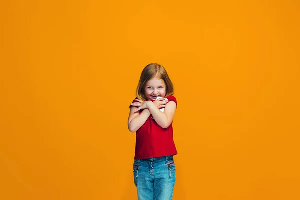 Den glada teen flicka står och ler mot orange bakgrund. — Stockfoto