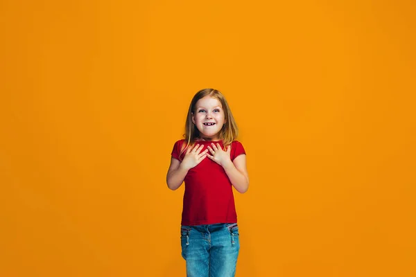 Den glada teen flicka står och ler mot orange bakgrund. — Stockfoto