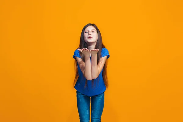 Den glada teen flicka står och ler mot orange bakgrund. — Stockfoto