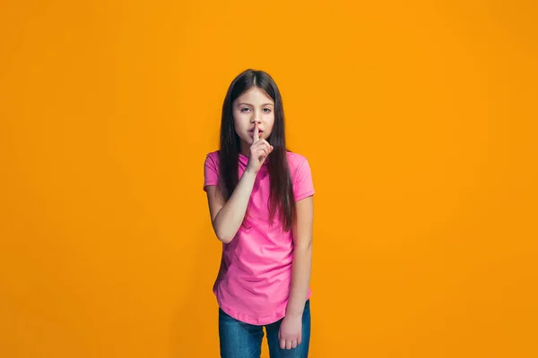 A jovem adolescente sussurrando um segredo atrás de sua mão sobre fundo laranja — Fotografia de Stock