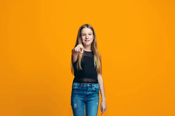 La chica adolescente feliz que apunta a usted, media longitud primer plano retrato sobre fondo naranja . — Foto de Stock