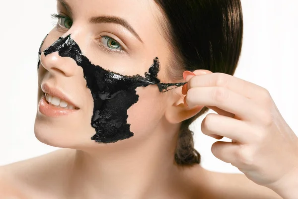 Молодая красивая женщина надевает маску на лицо терапевтической черной грязи. Лечение — стоковое фото