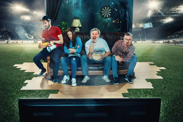 Futbolistas sentados en el sofá y viendo la televisión en medio de un campo de fútbol . — Foto de Stock