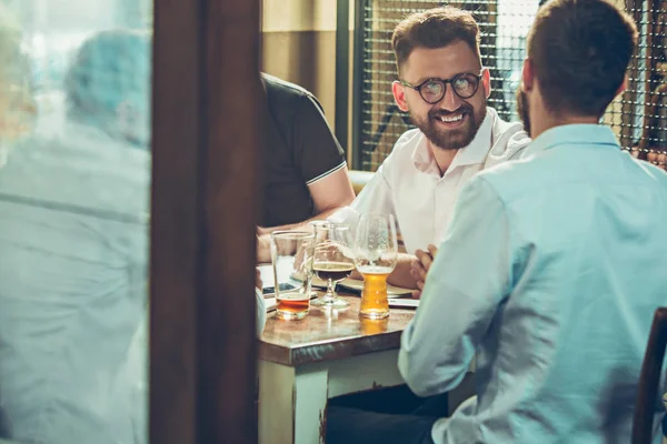 Los jóvenes alegres sonríen y hacen gestos mientras se relajan en el pub . — Foto de Stock