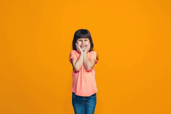 Den glada teen flicka står och ler mot orange bakgrund. — Stockfoto