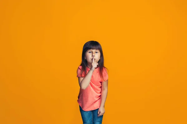 Den unga tonåring flicka viskar en hemlighet bakom hennes hand över orange bakgrund — Stockfoto