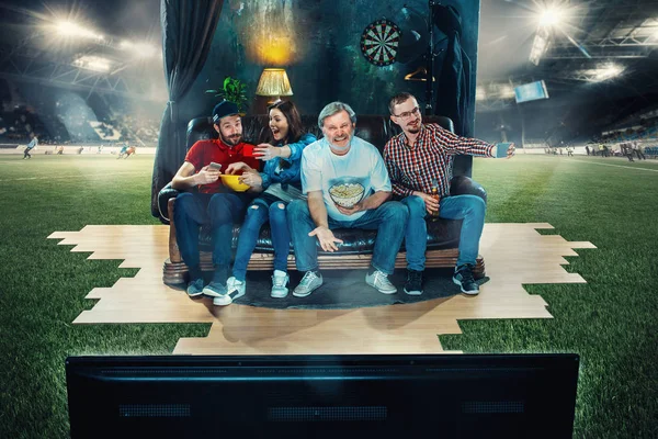 Futbolistas sentados en el sofá y viendo la televisión en medio de un campo de fútbol . — Foto de Stock
