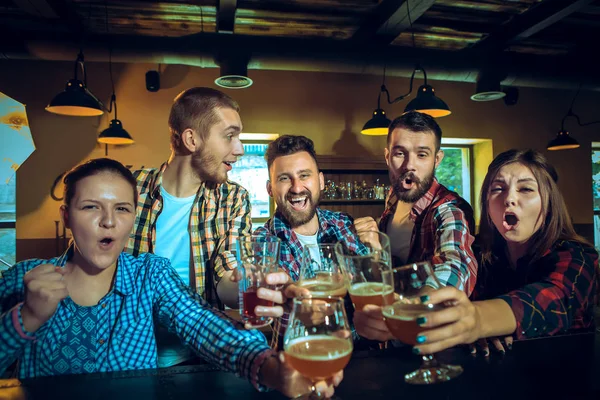 Sport, people, leisure, friendship and entertainment concept - happy football fans or male friends drinking beer and celebrating victory at bar or pub