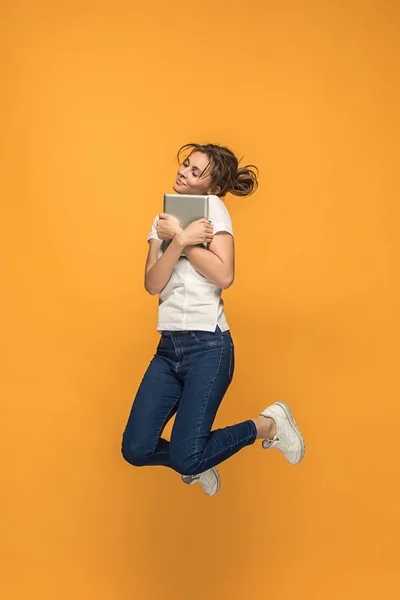 Imagen de mujer joven sobre fondo naranja usando computadora portátil o tableta gadget mientras salta . — Foto de Stock