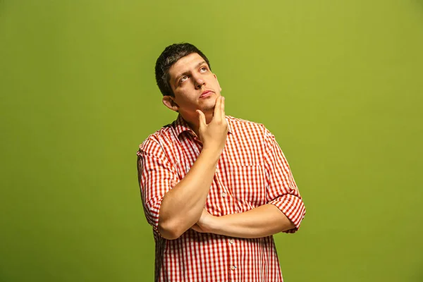 Let me think. Doubtful pensive man with thoughtful expression making choice against green background — Stock Photo, Image