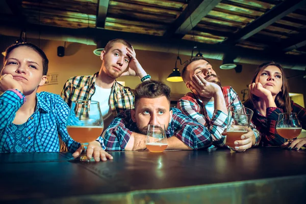 Des amis masculins et féminins bouleversés regardant un match de sport ou de football et buvant de la bière au bar ou au pub . — Photo