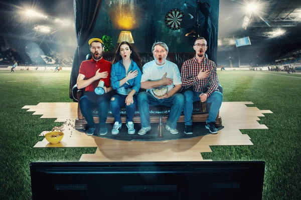 Fotboll Fotboll fläktar sitter i soffan och tittar på Tv mitt i en fotbollsplan. — Stockfoto