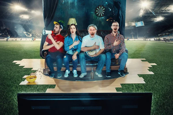 Fotboll Fotboll fläktar sitter i soffan och tittar på Tv mitt i en fotbollsplan. — Stockfoto