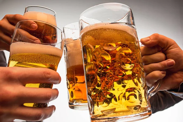 Manos con tazas de tostadas de cerveza creando salpicadura aislada sobre fondo blanco — Foto de Stock