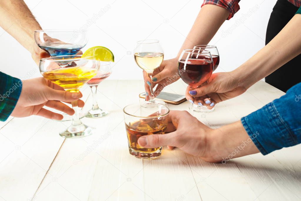 The side view of male and female hands with colorful exotic cocktails and fruits against white studio background. Toast, clinking glasses concept. Summer time concepts