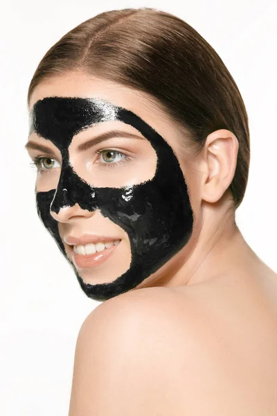 Jonge mooie vrouw een masker voor het gezicht van de therapeutische zwarte modder toe te passen. Spa-behandeling — Stockfoto
