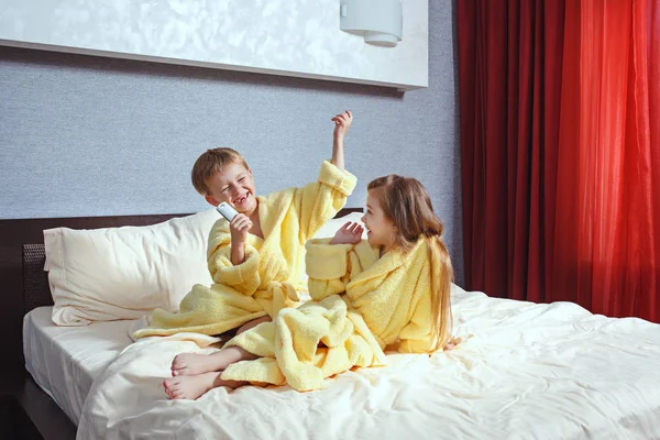 Happy laughing kids, boy and girl in soft bathrobe after bath play on white bed