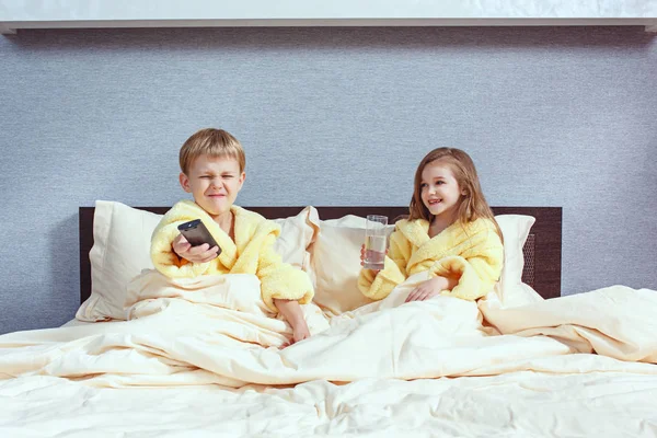 Feliz risa niños, niño y niña en suave albornoz después del juego de baño en la cama blanca —  Fotos de Stock