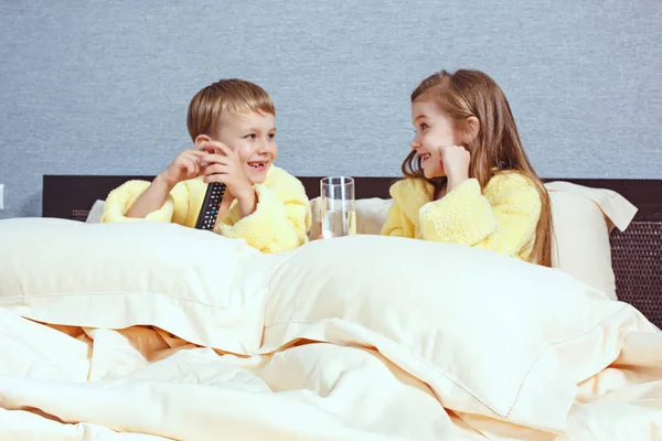 Boldog gyerekek nevetve, fiú és lány puha fürdőköpeny fürdő után játszani fehér ágy — Stock Fotó