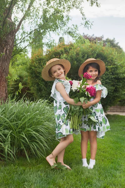 Retrato de meninas bonitas sorridentes com buquê de peônias contra grama verde no parque de verão . — Fotografia de Stock
