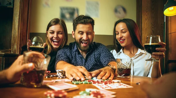 Foto vista lateral de amigos sentados à mesa de madeira. Amigos se divertindo enquanto joga jogo de tabuleiro . — Fotografia de Stock