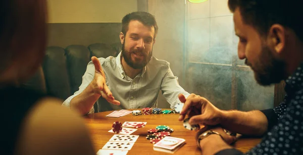 Foto vista lateral de amigos sentados à mesa de madeira. Amigos se divertindo enquanto joga jogo de tabuleiro . — Fotografia de Stock