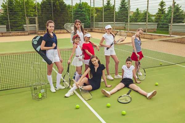 Portrait of group of girls as tennis players holding tennis racket against green grass of outdoor court