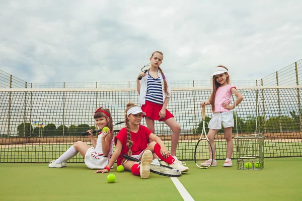 Portrait of group of girls as tennis players holding tennis racket against green grass of outdoor court