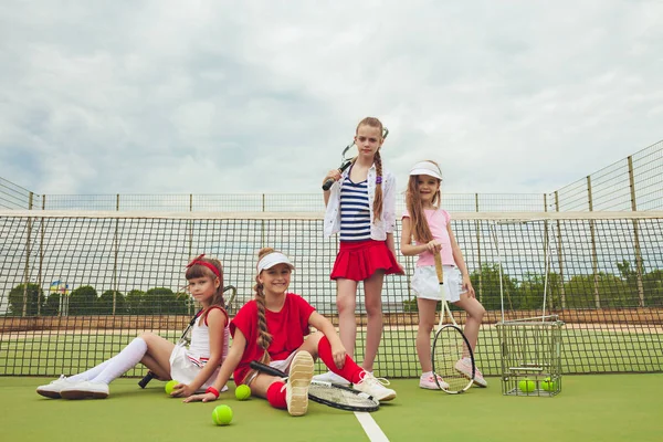 Retrato de grupo de meninas como tenistas segurando raquete de tênis contra a grama verde da quadra ao ar livre — Fotografia de Stock