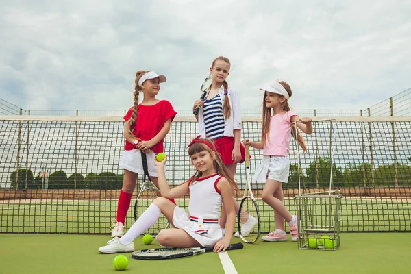 Portrait of group of girls as tennis players holding tennis racket against green grass of outdoor court