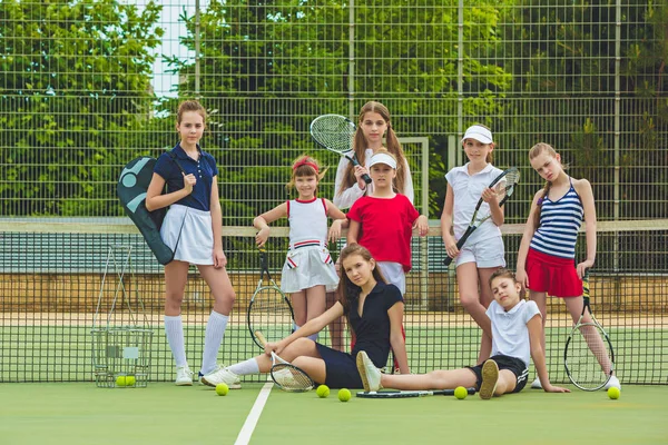 Portrait of group of girls as tennis players holding tennis racket against green grass of outdoor court