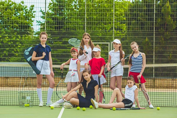 Portrait of group of girls as tennis players holding tennis racket against green grass of outdoor court