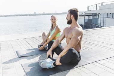 Fit fitness woman and man doing stretching exercises outdoors at city clipart