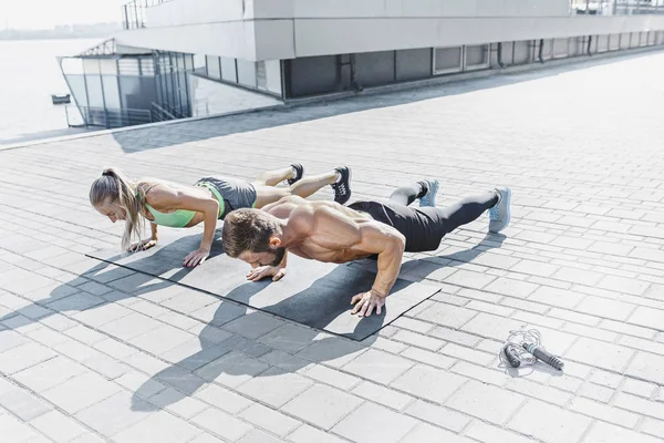 Fit fitness mujer y hombre haciendo ejercicios de fitness al aire libre en la ciudad — Foto de Stock