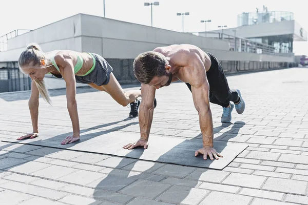 Fit fitness mujer y hombre haciendo ejercicios de fitness al aire libre en la ciudad —  Fotos de Stock