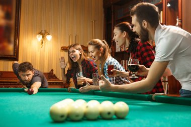 Young men and women playing billiards at office after work. clipart
