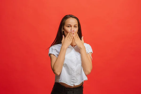 The young woman whispering a secret behind her hand over red background — Stock Photo, Image