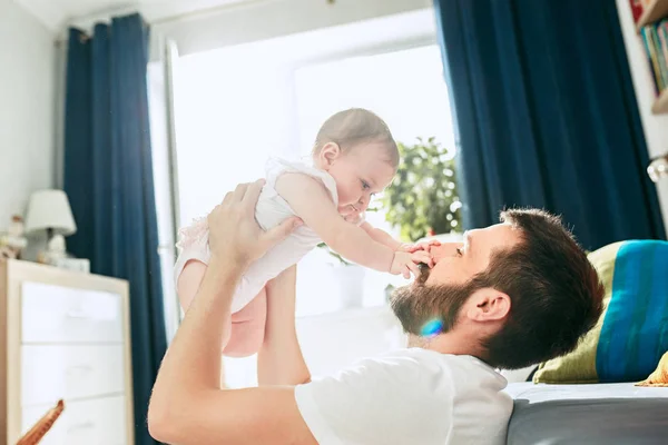 Proud father holding his newborn baby daughter up in the air at home — Stock Photo, Image