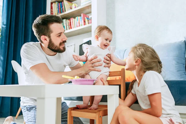 Hombre joven bien parecido desayunando y alimentando a su bebé en casa — Foto de Stock