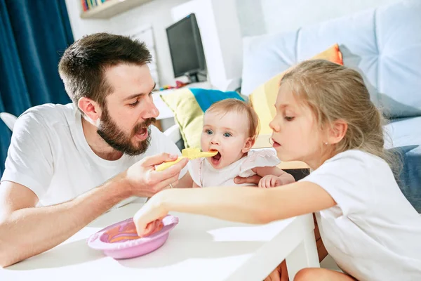 Dobry patrząc młody człowiek jedzenie śniadanie i karmienie jej córeczkę w domu — Zdjęcie stockowe