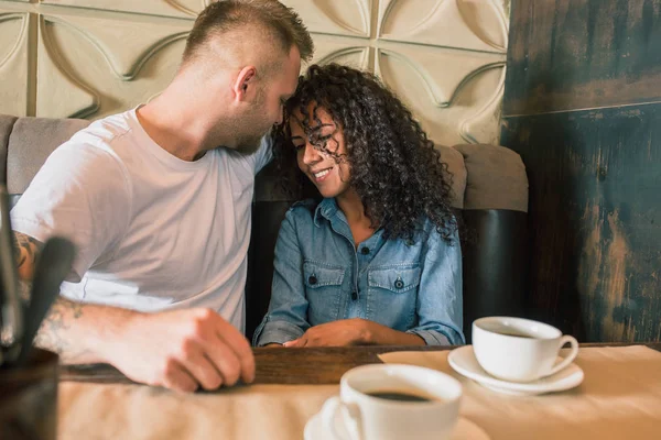 Feliz joven pareja está bebiendo café y sonriendo mientras se sienta en el café —  Fotos de Stock