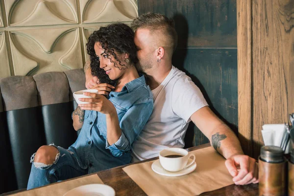 Feliz joven pareja está bebiendo café y sonriendo mientras se sienta en el café —  Fotos de Stock