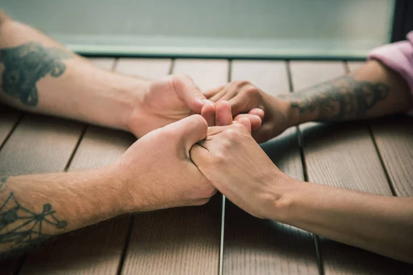Close up on a man and a woman holding hands at a wooden table — Stock Photo, Image